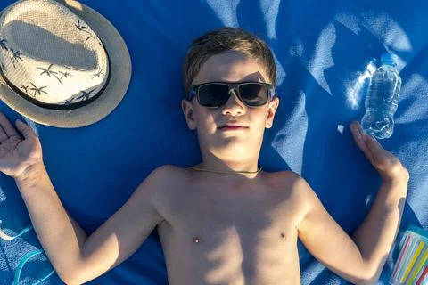 Happy boy in sunglasses with bare torso sunbathing lying on the beach 库存照片