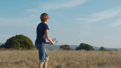 Happy boy throwing paper plane outdoors on sunny day Stock Footage 129423598