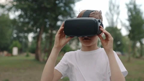 Happy boy in virtual reality glasses plays video games outdoors. 库存影片 196628115