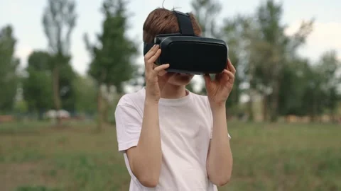 Happy boy in virtual reality glasses plays video games outdoors. Stock Footage 196628138