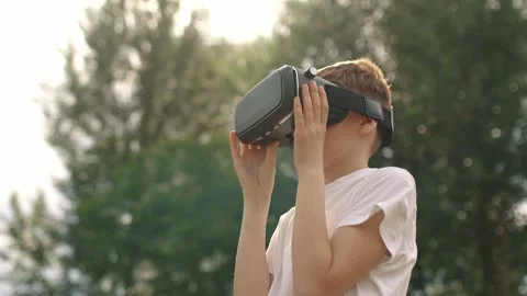 Happy boy in virtual reality glasses plays video games outdoors. Stock Footage 196628234
