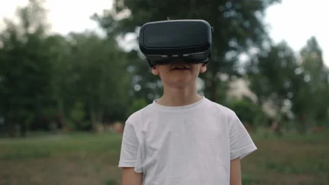 Happy boy in virtual reality glasses plays video games outdoors. 動画素材 197272613