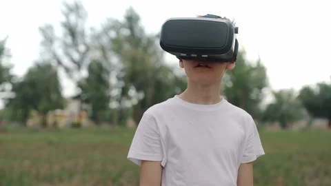 Happy boy in virtual reality glasses plays video games outdoors. Video stock 197272684