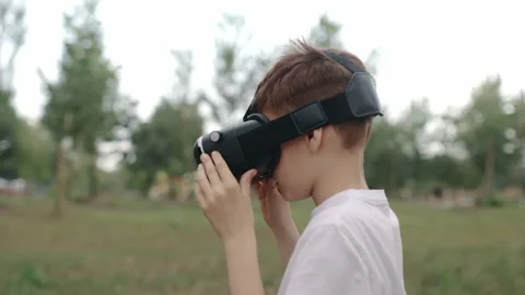 Happy boy in virtual reality glasses plays video games outdoors. Stockbeeldmateriaal 197272768