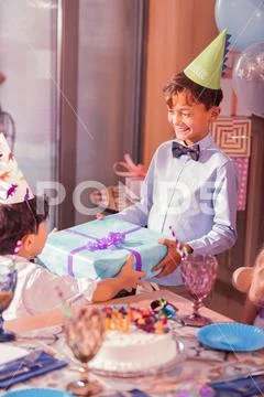 Happy boy wearing party hat and giving present to his friend Stock Photos
