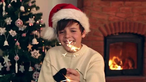 Happy boy wearing a santa hat laughing and waving with christmas sparkler Stock Footage 80299036