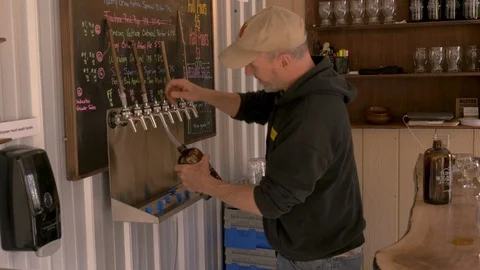 Happy brewmaster bartender filling a growler with beer at a small craft brewery Stock Footage