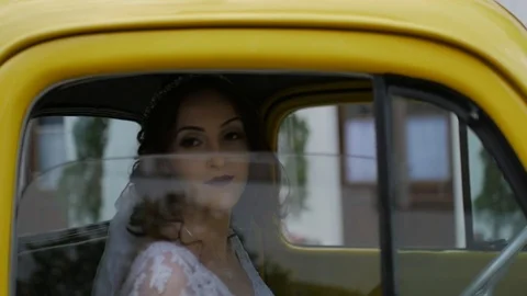 Happy bride going away inside a retro yellow ford car Stock Footage 89559425