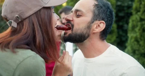 Happy brunette guy with a beard bites a barbecue sausage together with his Stock Footage 283832632