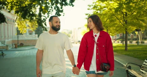 A happy brunette guy with a beard walks with his brunette girlfriend in a red Stock Footage 280574650