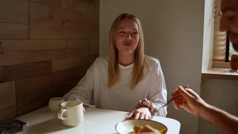 A happy brunette guy in a pink jacket feeds his blonde girlfriend with a fork Vídeos de archivo 295395796