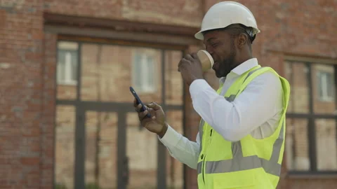 Happy builder with smartphone and cup of coffee outdoors Stock Footage 200922660