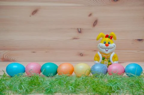 Happy bunny with easter eggs and grass on the wooden background Stock Photos