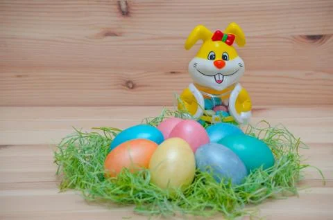 Happy bunny with easter eggs in a nest on the wooden background Stock Photos