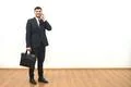 The happy businessman with a briefcase phones on the white wall background Photo