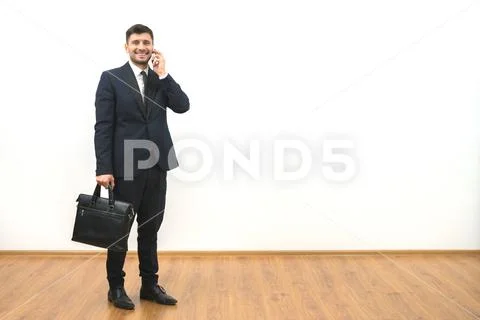 The happy businessman with a briefcase phones on the white wall background Stock Photos