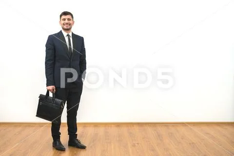 The happy businessman with a briefcase standing on the white wall background Stock Photos