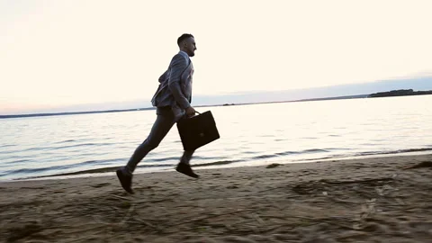 Happy businessman holding in hand briefcase and running on the beach at sunset. Stock Footage 118317280