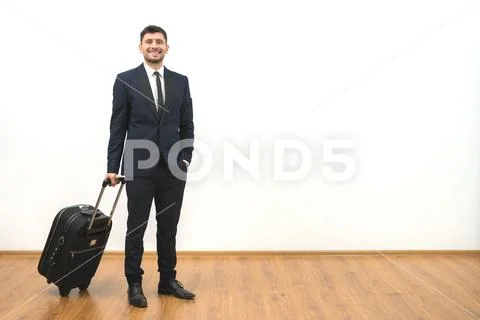 The happy businessman with a suitcase standing on the white wall background Stock Photos