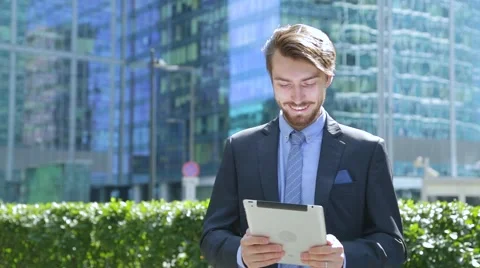 Happy businessman is using tablet computer near the modern business center Stock Footage 67583119