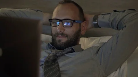 Happy businessman watching movie on laptop on bed in hotel room at night Stock Footage