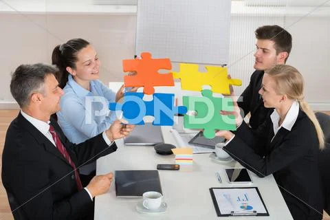 Happy Businesspeople Joining Multicolored Puzzle Piece In Meeting Stock Photos