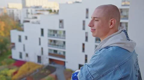 Happy casually dressed queer non-binary person standing on balcony and softly Stock Photos