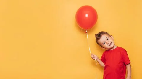 A happy Caucasian boy isolated on a bright yellow background holds a red balloon Stock Photos