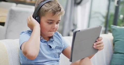 Happy caucasian boy sitting on sofa and using tablet, slow motion Stock Footage 337096361