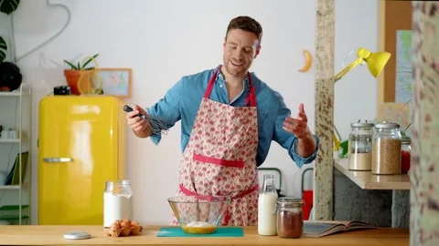 Happy Caucasian guy smiling while mixing eggs with flour in glass bowl at cozy Stock Footage 114915152