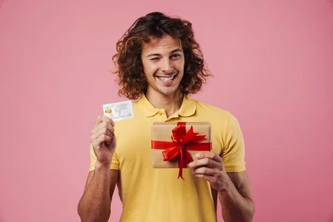 Happy caucasian guy winking while showing gift box and credit card Stock Photos