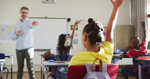 Happy caucasian male teacher in classroom with children raising hands during Stock Footage
