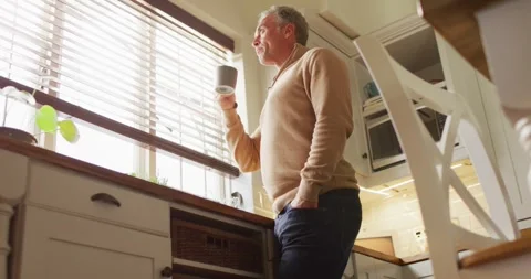 Happy caucasian man looking through window and drinking coffee in kitchen Stock Footage 335268526