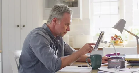 Happy caucasian man sitting at table in kitchen, using tablet Video stock 342798256
