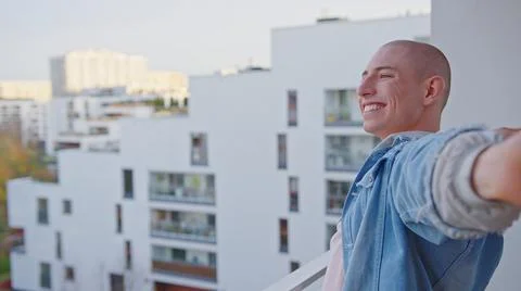 Happy caucasian queer non-binary person standing on balcony and smiling. Stock Photos