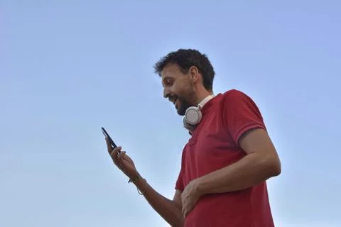 Happy Caucasian young man, wearing white headset, using smart phone Stock Photos