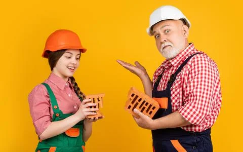Happy child and grandfather bricklayer in hard hat on yellow background Stock Photos