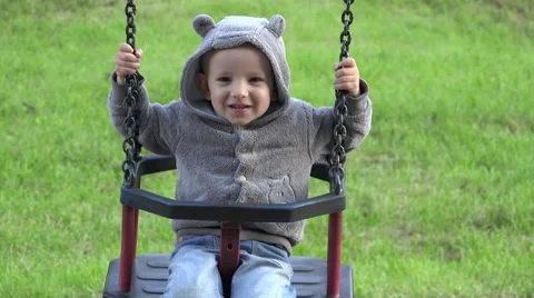 Happy child balancing in swing playing hide and seek, hiding face with hands  Video stock 46207489