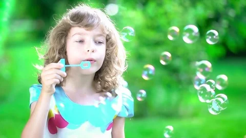 Happy child blowing soap bubbles in spring park. Slow motion Stock Footage 71668431