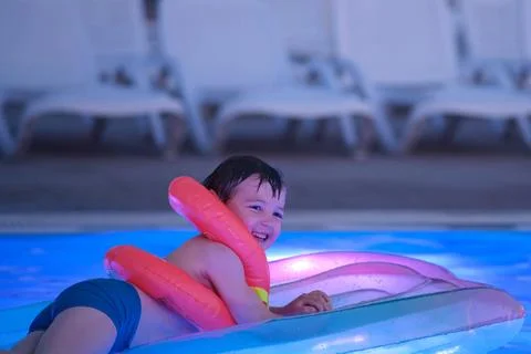 Happy child boy with inflatable ring swimming on air mattress in pool at ni.. Fotos de archivo