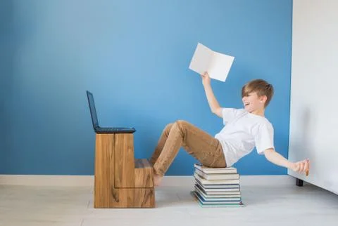 Happy child boy sitting on stack of books with his laptop, studying online at Stock Photos