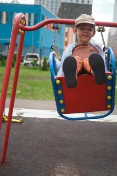 Happy child boy swinging on playground swing in city park. Small male kid p.. Stock Photos
