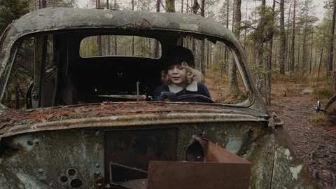 A happy child with curly hair drives an old rusty car in a car graveyard Stock Footage
