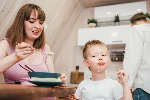 Happy child eats pasta in the kitchen with her family Stock Photos