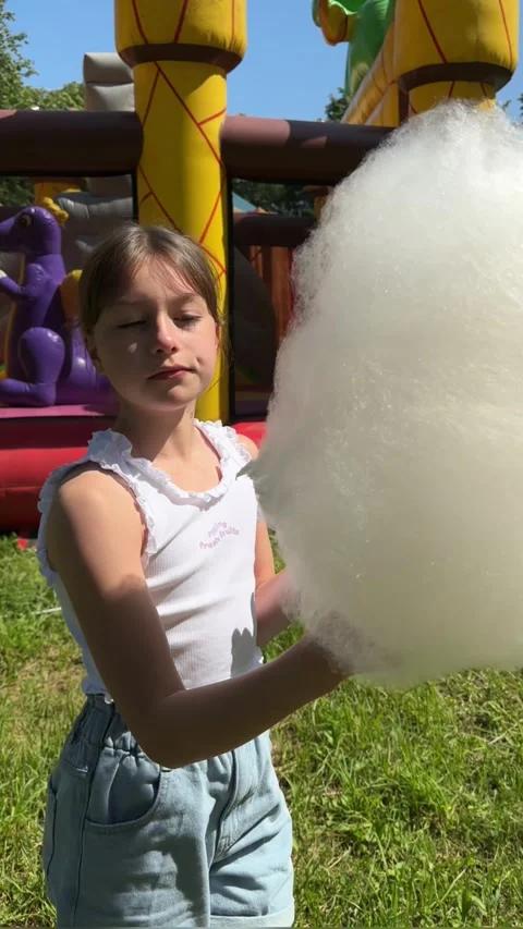 A happy child eats sweet cotton candy at an amusement park on a summer day, Stock Footage 244326519