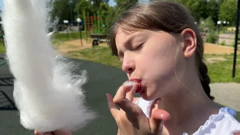 A happy child eats sweet cotton candy at an amusement park on a summer day, Stock Footage 244326537