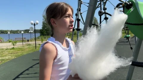 A happy child eats sweet cotton candy at an amusement park on a summer day, Stock Footage 244326583