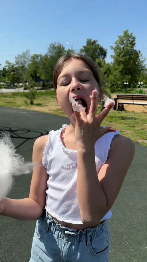 A happy child eats sweet cotton candy at an amusement park on a summer day, a Stock Footage 244326663