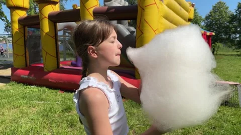 A happy child eats sweet cotton candy at an amusement park on a summer day, 스톡 동영상 244660668
