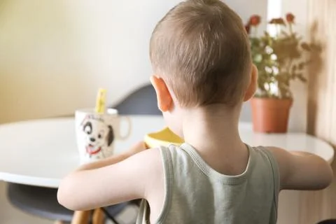 Happy child eats at the table by himself. Healthy food, back view Stock-Fotos